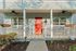 Charming front porch with a vibrant red door, inviting white railing, and welcoming pathway surrounded by lush greenery.