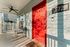 Charming apartment entry with a vibrant red door, set against soothing grey siding, featuring a cozy porch with chic chairs and a ceiling fan.