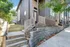 Modern townhouse exterior with sleek metal siding, brick accents, and inviting entry steps, surrounded by lush greenery.