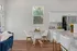 Modern kitchen and dining area with white cabinetry, round glass table, and sleek chairs, enhanced by natural light and vibrant decor.