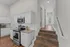 Charming kitchen with modern stainless steel appliances, sleek white cabinetry, and inviting wood flooring leads to a spacious hallway.