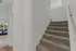 Inviting entryway with plush carpeted stairs leading to a bright living area with large windows and a stylish blue sofa.