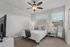 Chic bedroom showcasing a cozy queen bed, elegant ceiling fan, modern decor, and ample natural light through large windows.