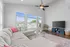 Bright and airy living room featuring a plush sectional sofa, large windows with scenic views, a modern ceiling fan, and a stylish entertainment unit.