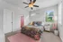 Charming bedroom with a colorful bedspread, bright natural light from multiple windows, and modern ceiling fan.