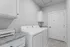 Modern laundry room with sleek white washer and dryer, granite countertop, and elegant cabinetry.