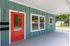 Charming home entrance with vibrant red door, modern teal siding, and sleek house number display, offering a welcoming curb appeal.