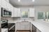Bright and modern kitchen featuring sleek stainless steel appliances, pristine white cabinetry, and ample counter space with a view of lush greenery through the window.