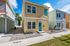 Charming two-story, pastel-colored homes with welcoming front porches, bright blue doors, and beautifully maintained landscapes under a clear blue sky.