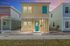 Charming two-story yellow home with blue accents and a welcoming turquoise door, set against a beautiful sunset sky.