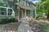 Charming duplex with rustic wooden doors, lush landscaping, and inviting walkway under a canopy of mature trees.