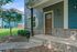 Charming front entrance of a modern home with a rustic wooden door, elegant brickwork, and lush green landscaping.