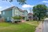 Charming green two-story house with modern design, nestled in a serene neighborhood with lush greenery and tree-lined street.