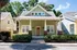 Charming green house with a welcoming front porch and lush landscaping, perfect for suburban tranquility.