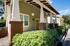 Charming bungalow exterior with elegant columns, lush green shrubs, and a welcoming porch under a clear blue sky.