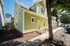 Charming two-story house with a green exterior, featuring large windows and a welcoming pathway adorned by lush trees.