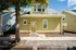 Charming green house with a welcoming front porch, nestled in a tree-lined neighborhood under a bright blue sky.