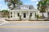 Charming white cottage with a welcoming front porch, nestled on a corner lot with lush greenery and classic architecture.