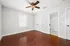 Bright and inviting bedroom featuring sleek hardwood floors, a stylish ceiling fan, and an ensuite bathroom with modern subway tiles.