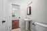 Bright bathroom with modern pedestal sink and elegant lighting, featuring a view into a sunny room with rich hardwood floors.