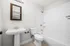 Bright, contemporary bathroom featuring a sleek pedestal sink, elegant wood-framed mirror, and pristine white subway tiles for a modern touch.