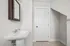 Bright and inviting bathroom with a sleek white pedestal sink and stylish dark wood framed mirror, complemented by a clean white door and modern tile flooring.