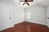 Bright and airy room with elegant wooden flooring, a ceiling fan, and a large window, perfect for a cozy bedroom or home office.