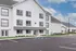 Modern apartment complex showcasing clean white exterior, ample parking, and bright windows under a clear blue sky.