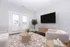 Contemporary living room with elegant decor, featuring a large wall-mounted TV, stylish wooden coffee table, plush seating, and vibrant natural light through French doors.