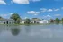 Scenic lakefront apartment complex surrounded by lush greenery under a clear blue sky.