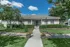 Charming single-story apartment with manicured lawns, lush greenery, and inviting entrance under a clear blue sky.