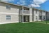 Charming two-story apartment building with private balconies and lush green lawns under a bright blue sky.