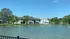 Scenic lakeside view of charming apartment buildings with balconies, nestled among lush greenery under a clear blue sky.