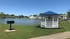 Tranquil apartment complex view featuring a serene pond, charming white gazebo, and spacious green lawn with vibrant trees.