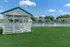 Charming lakeside gazebo overlooking serene water, surrounded by lush greenery and modern apartment buildings under a clear blue sky.