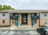 Charming two-story apartment building with brick facade and inviting teal doors, offering a peaceful residential setting surrounded by lush greenery.