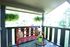 Charming balcony with a vibrant red bench, colorful cushions, and lush hanging plants overlooking a serene green landscape.