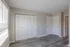 Bright and spacious bedroom featuring modern grey hardwood floors, large closet with white louvered doors, and abundant natural light streaming through wide windows.