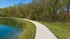 Scenic view of a serene walking path curving alongside a tranquil lake and lush, green forest.