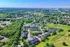 Scenic aerial view of a vibrant community surrounded by lush greenery, featuring modern apartment complexes with convenient city access in the background.