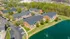 Charming residential complex with brick buildings and lush greenery, overlooking a serene pond with a water feature.