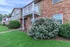 Charming brick apartment exterior with a quaint balcony, lush green lawn, and vibrant garden shrubs, creating an inviting and serene atmosphere.