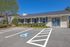 Charming single-story building with blue shutters, accessible parking, and lush landscaping under a clear blue sky.