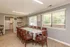 Bright dining area with elegant wood chairs surrounding a large table, featuring large windows and a modern open-concept kitchen.