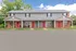 Charming townhouse duplex with vibrant red doors and welcoming front patios, set against lush greenery and clear blue skies.