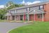 Charming duplex with red brick accents and vibrant red doors, nestled in a lush green setting.