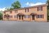 Charming brick townhouse with cozy entrances and vibrant shutters, surrounded by lush greenery and a clear blue sky.