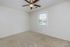 Bright and inviting room with fresh neutral decor, plush carpet, and a modern ceiling fan, offering serene views through a large window.