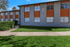 Charming exterior view of a modern apartment building with vibrant orange accents, lush green lawn, and large windows inviting natural light.