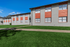 Bright and inviting apartment complex with modern fa&ccedil;ade, featuring vibrant orange accents and lush green lawns under a clear blue sky.
